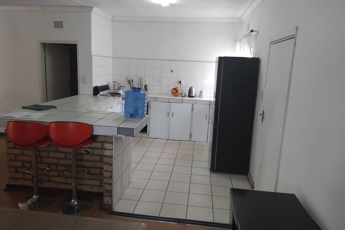 A functional kitchen featuring a brick breakfast bar, tiled countertops, and white cabinetry, offering a practical layout with potential for modern updates.