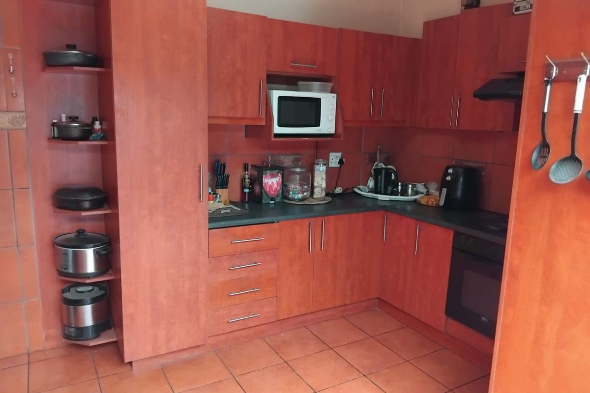 A functional kitchen featuring warm-toned laminate cabinetry, built-in oven, extractor fan, and tiled flooring with a practical layout.