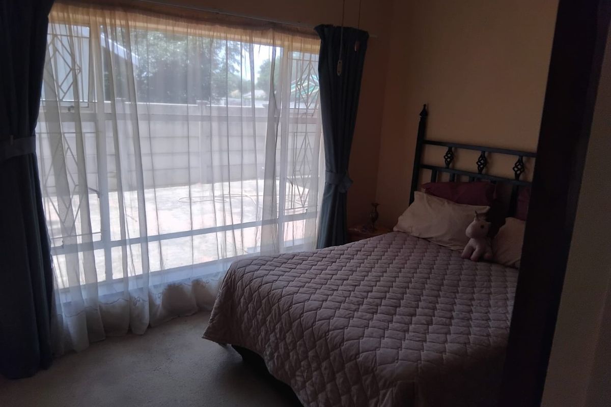 A bedroom featuring a large window with security gate and carpeted flooring, offering natural light and a view of the exterior area.
