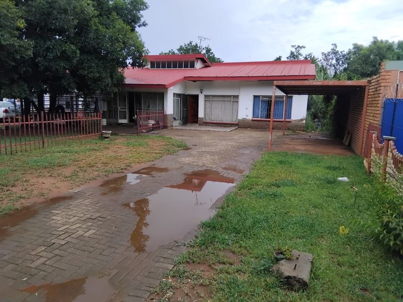 Front exterior view of a single-story house featuring a red corrugated metal roof, paved driveway, and an attached carport.