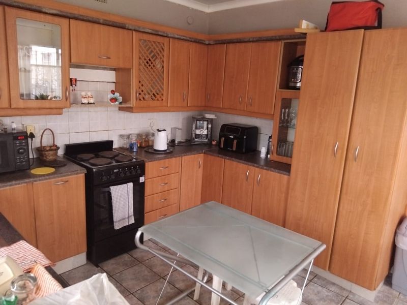 A functional kitchen featuring wood-look laminate cabinetry, tiled backsplash, and a freestanding electric stove with ample storage space.