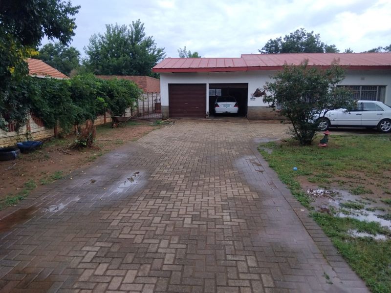Front view of the property featuring a paved driveway leading to a double garage with a metal roof and surrounding boundary wall.