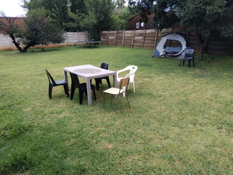 A spacious backyard garden featuring a large lawn area enclosed by a precast concrete boundary wall.