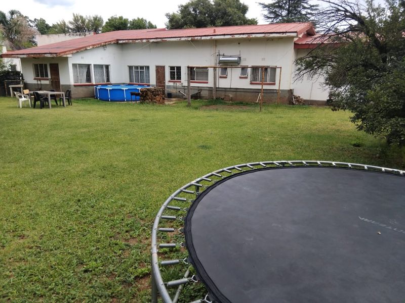 Rear view of the property featuring a large lawn area and a single-story building with a metal roof and solar water heating system.