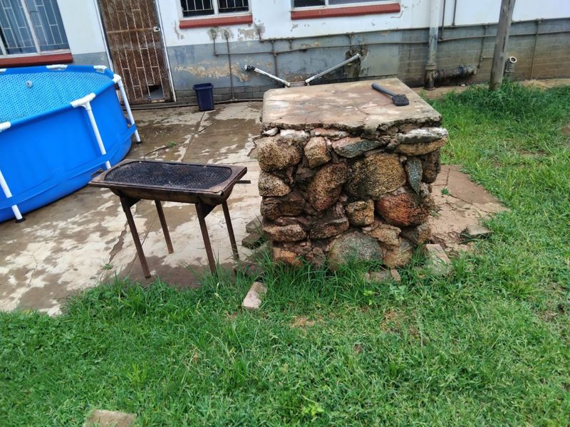 Rear exterior area featuring a stone masonry pillar, concrete paving, and visible exterior wall maintenance requirements.