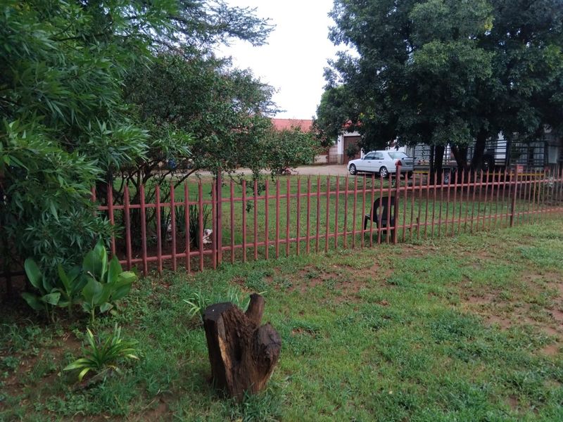 A view of the property garden featuring a lawn, mature trees, and metal perimeter fencing.