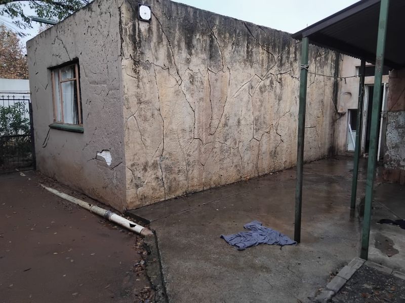 Rear exterior view of the property showing a concrete patio area and a structure with significant wall cracking and surface deterioration.