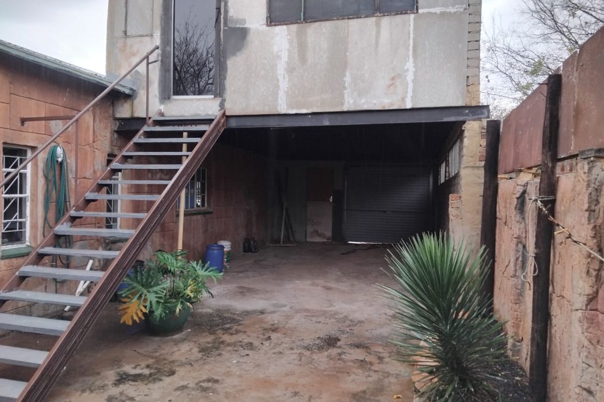 Rear exterior view showing a metal staircase leading to an upper level, a ground-level garage area, and weathered stone cladding.