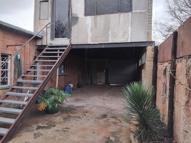 Rear exterior view showing a metal staircase leading to an upper level, a ground-level garage area, and weathered stone cladding.