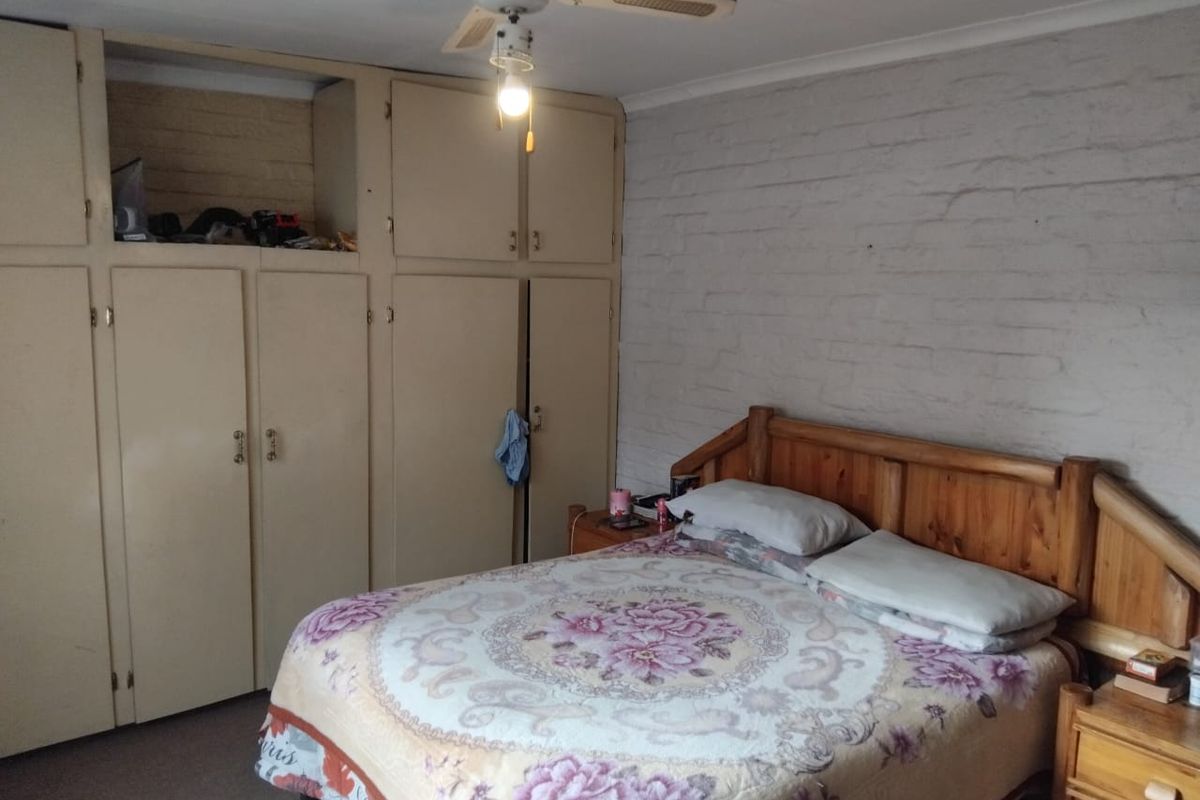 Bedroom featuring built-in cupboards, a ceiling fan, and a textured exposed brick wall finish.
