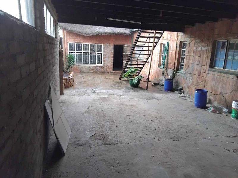 A covered outdoor patio area featuring exposed brickwork, a metal staircase, and concrete flooring, offering potential for renovation and improved outdoor living space.