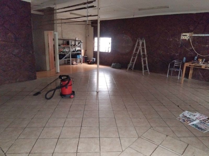 An open-plan living area featuring tiled flooring and textured stone-effect wall cladding, currently in a vacant state requiring cosmetic updates.