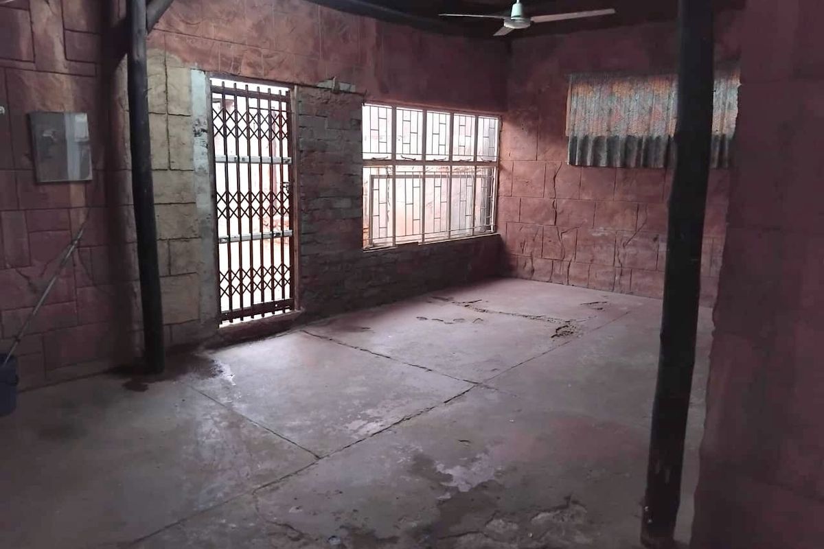 An empty living area featuring exposed timber beams, stone-effect wall cladding, and a security gate, requiring significant cosmetic updates to the flooring and walls.