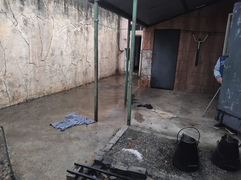 A weathered rear patio area featuring a concrete floor, metal support structure, and a solid metal door, requiring maintenance and cosmetic updates.