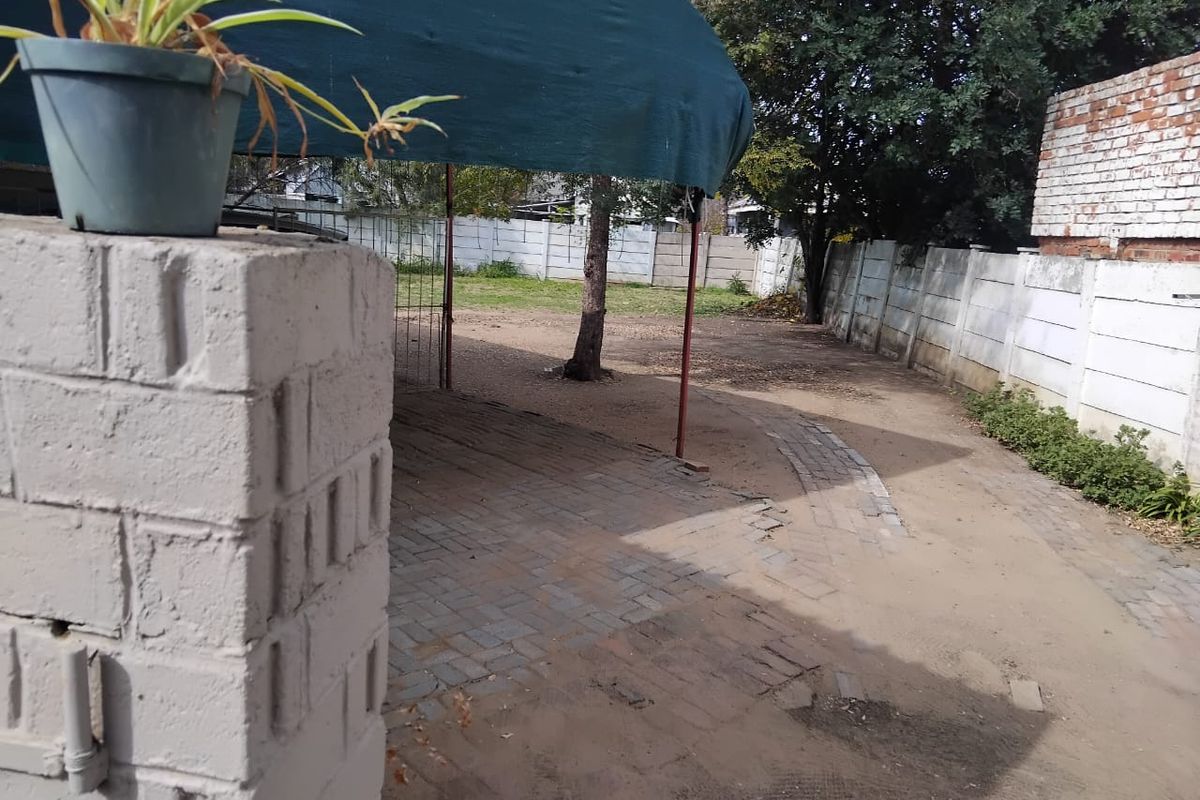 Rear outdoor area featuring a paved section, a fabric shade structure, and perimeter precast concrete walling.