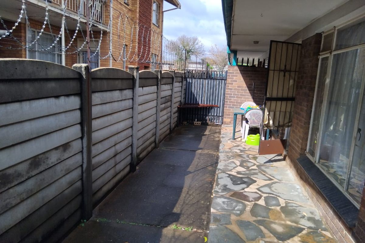 A rear exterior area featuring a paved patio, brick building facade, and a precast concrete boundary wall topped with security razor wire.