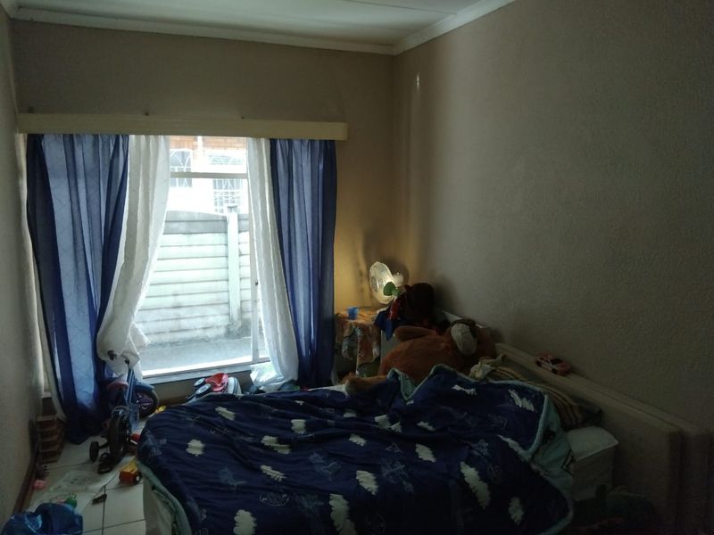 A bedroom featuring tiled flooring and a sliding window with curtain fixtures, providing natural light and access to the exterior.