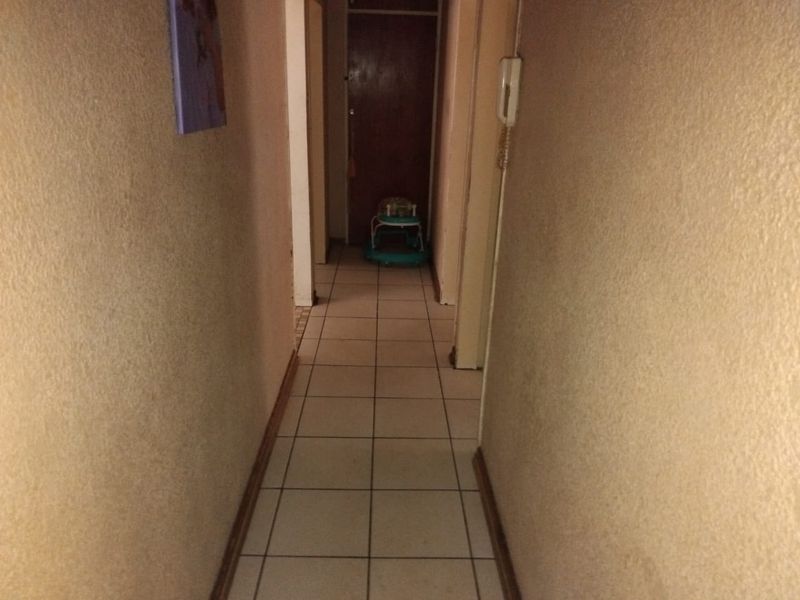 A narrow residential hallway featuring tiled flooring and a wall-mounted intercom system, providing access to various rooms within the apartment.