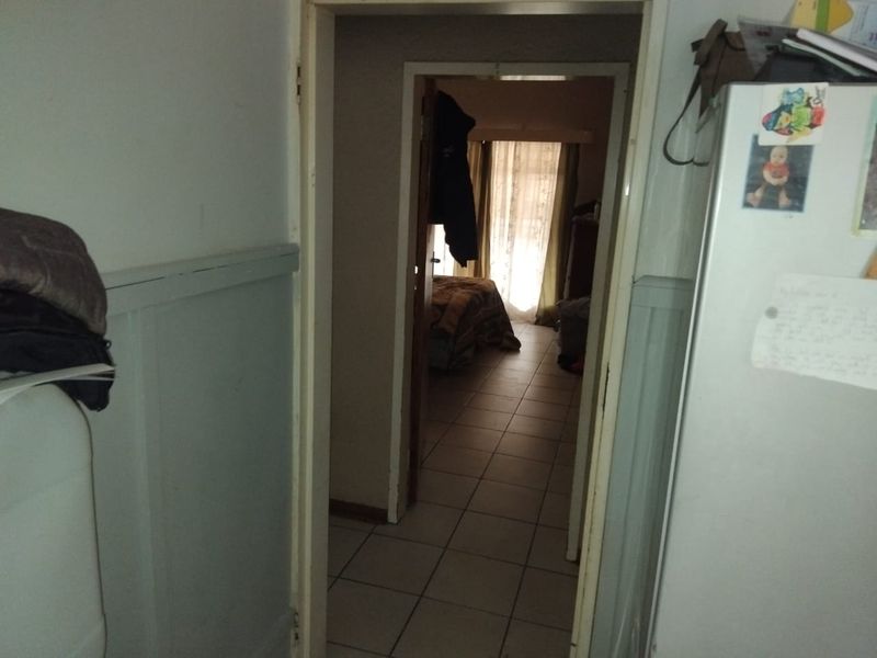 A view through a doorway into a tiled hallway leading towards a bedroom area with natural light.
