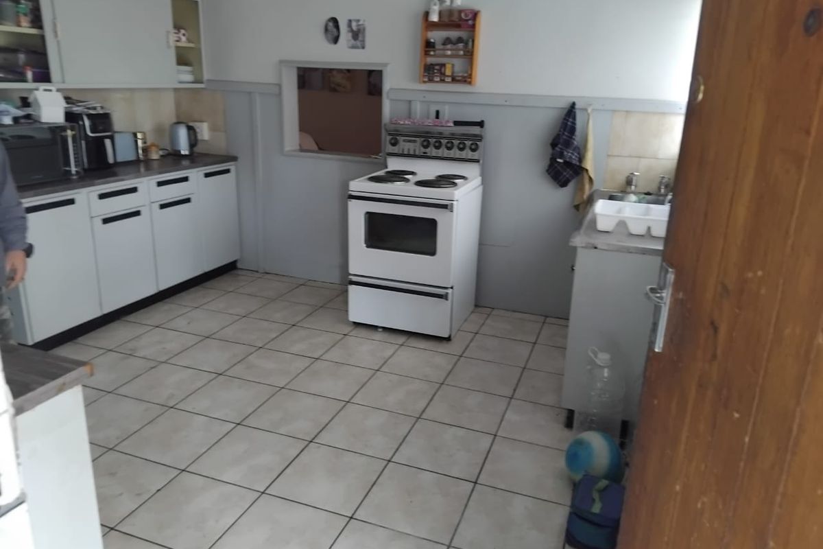 A functional kitchen featuring white cabinetry, a freestanding stove, tiled flooring, and a convenient pass-through window connecting to the adjacent living space.