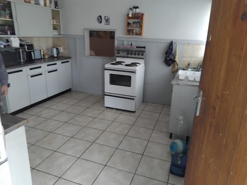 A functional kitchen featuring white cabinetry, a freestanding stove, tiled flooring, and a convenient pass-through window connecting to the adjacent living space.