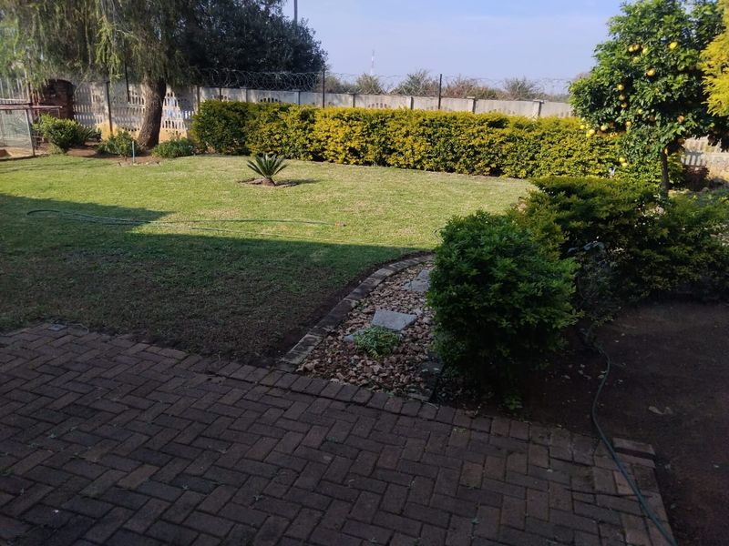 A well-maintained private garden featuring a paved patio area, established lawn, mature shrubs, and a perimeter wall with security fencing.