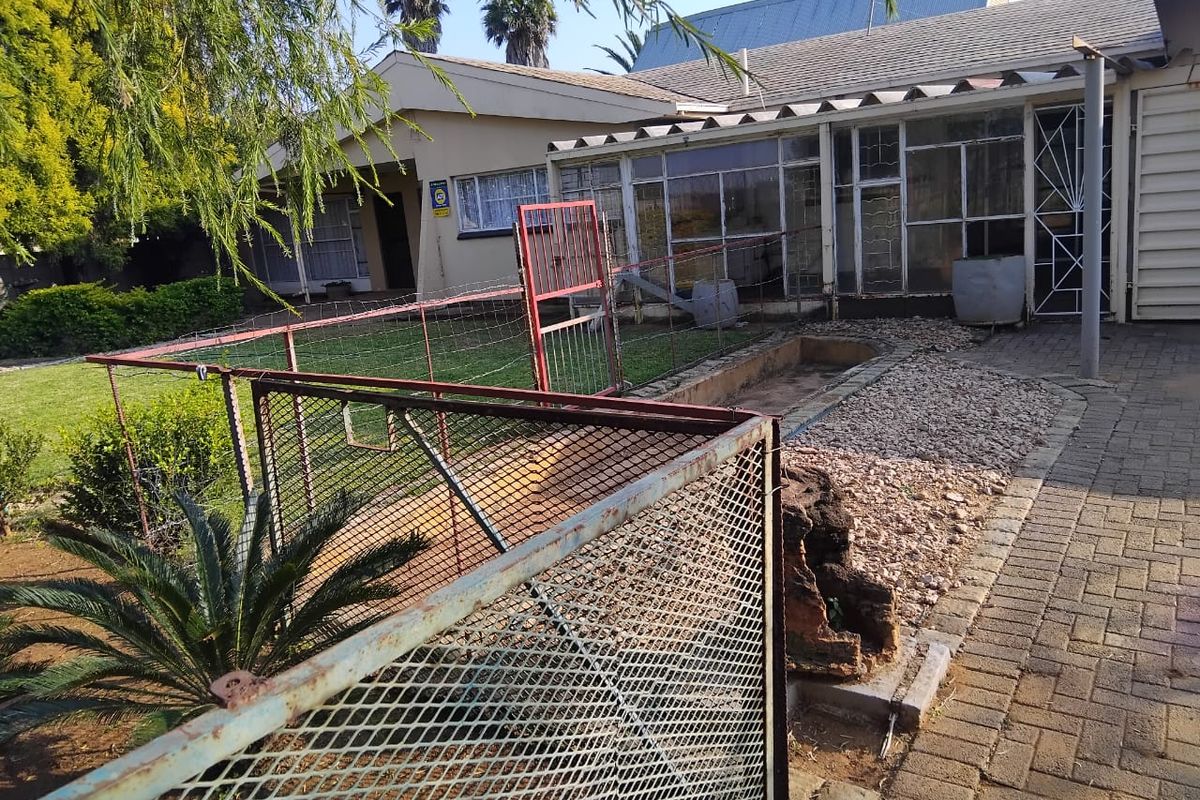 Rear exterior view of the property featuring a paved area, enclosed patio, and metal security fencing in need of maintenance.