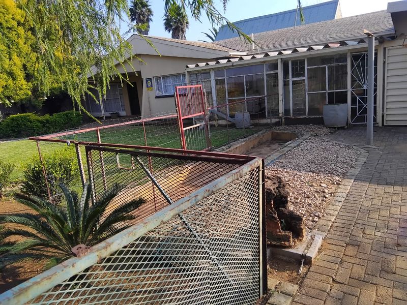 Rear exterior view of the property featuring a paved area, enclosed patio, and metal security fencing in need of maintenance.