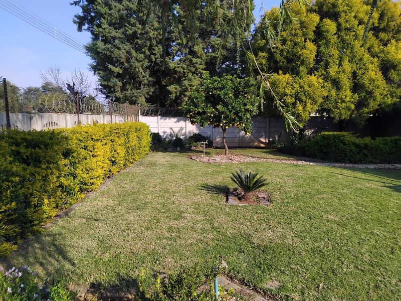 A well-maintained private garden featuring a manicured lawn, established fruit trees, and secure perimeter walling with razor wire.