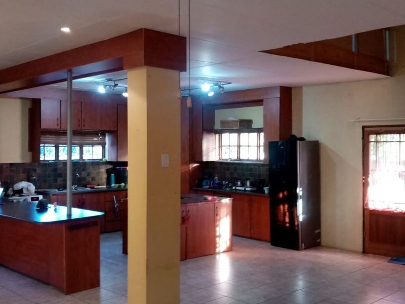 Spacious open-plan kitchen and living area featuring wooden cabinetry, a central island, tiled flooring, and direct access to the exterior via double doors.