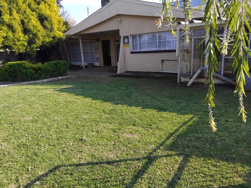 Rear view of the house featuring a spacious lawn, paved patio area, and established garden surroundings.
