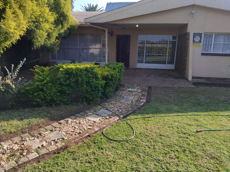 Front elevation of the house featuring a covered entrance, security bars on windows, and a landscaped garden with a paved walkway.