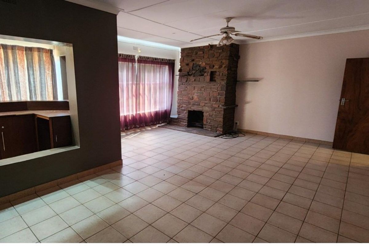 Spacious living room featuring a prominent brick fireplace, tiled flooring, and a convenient pass-through window connecting to the adjacent kitchen area.