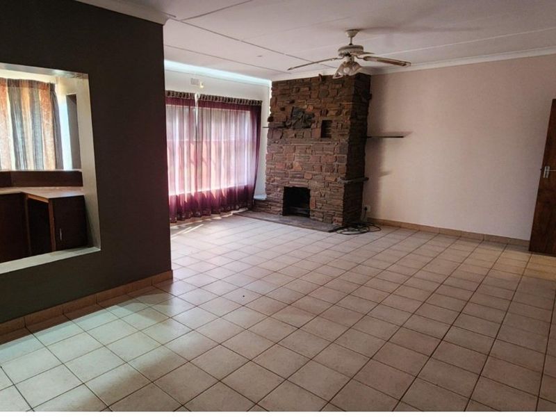 Spacious living room featuring a prominent brick fireplace, tiled flooring, and a convenient pass-through window connecting to the adjacent kitchen area.