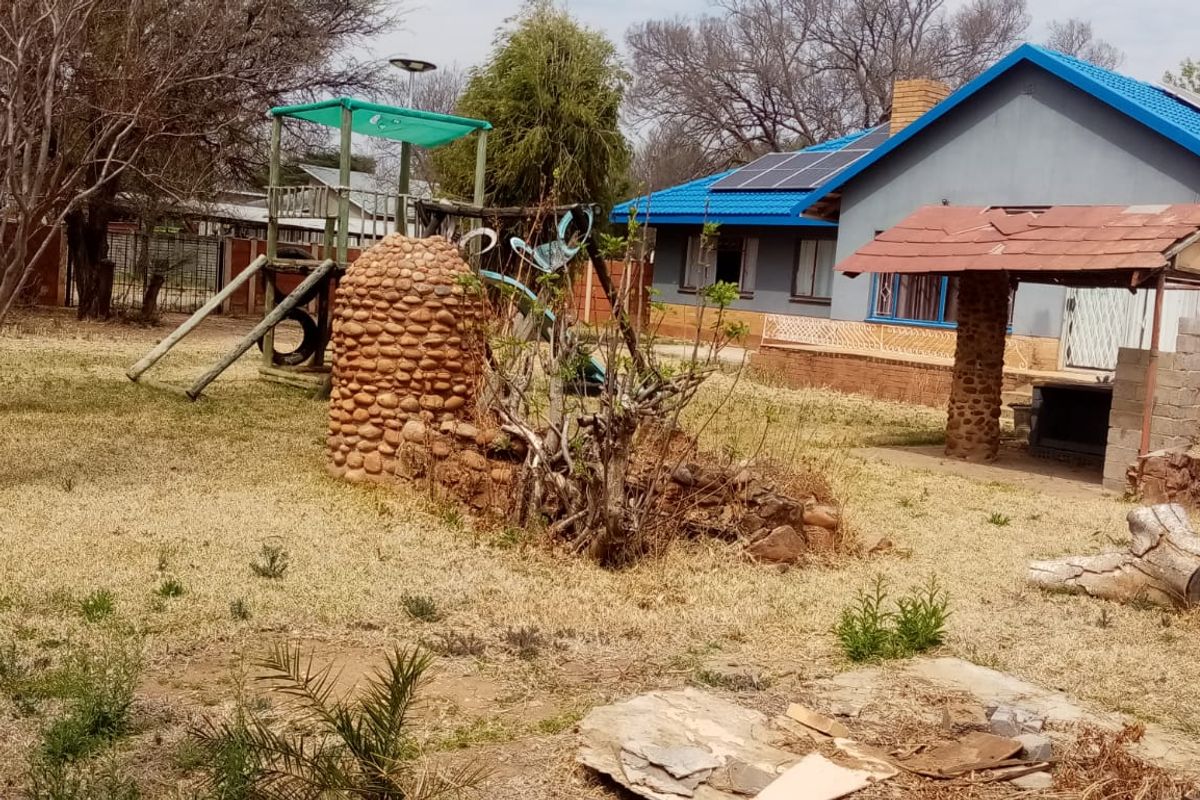 Spacious rear garden featuring a covered patio with a built-in braai, stone-clad features, and solar panels installed on the main house roof.
