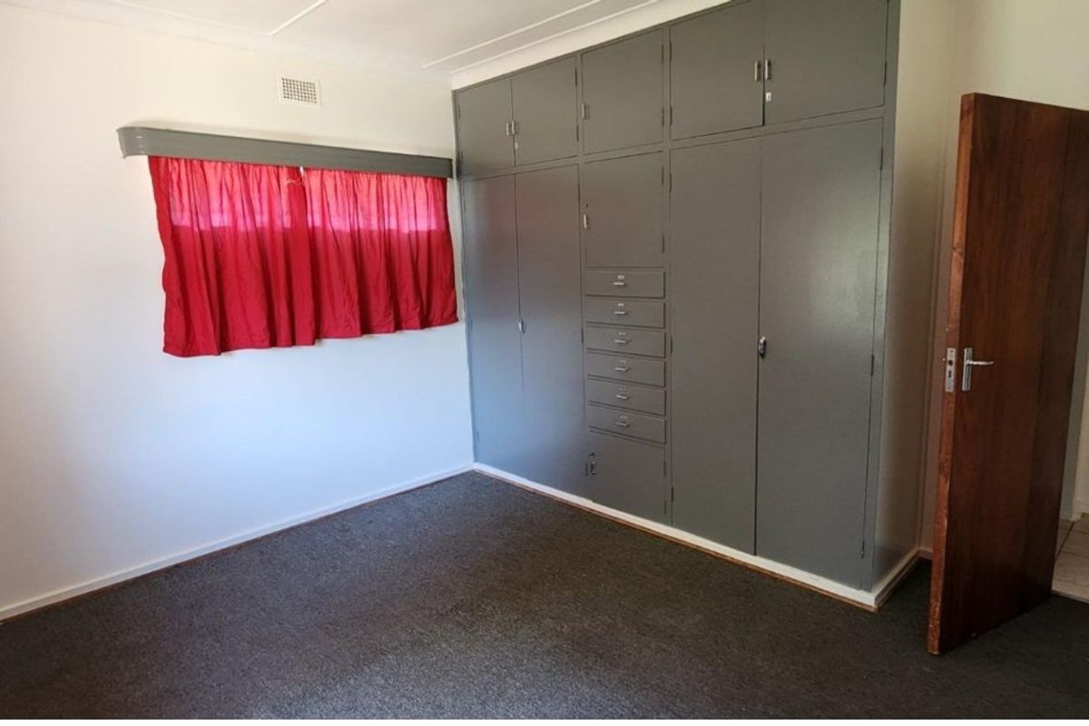 A vacant bedroom featuring extensive built-in grey cabinetry, carpeted flooring, and a wooden door, offering a blank canvas for potential updates.