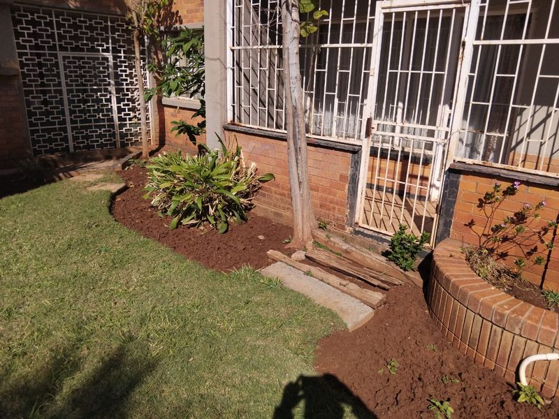 A rear garden area featuring a brick facade, security gates, and a built-in brick planter box with established lawn and garden beds.