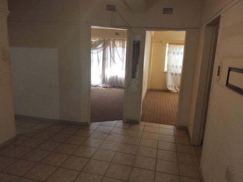 A view from a tiled hallway looking into two carpeted rooms, featuring exposed wiring and dated interior finishes.