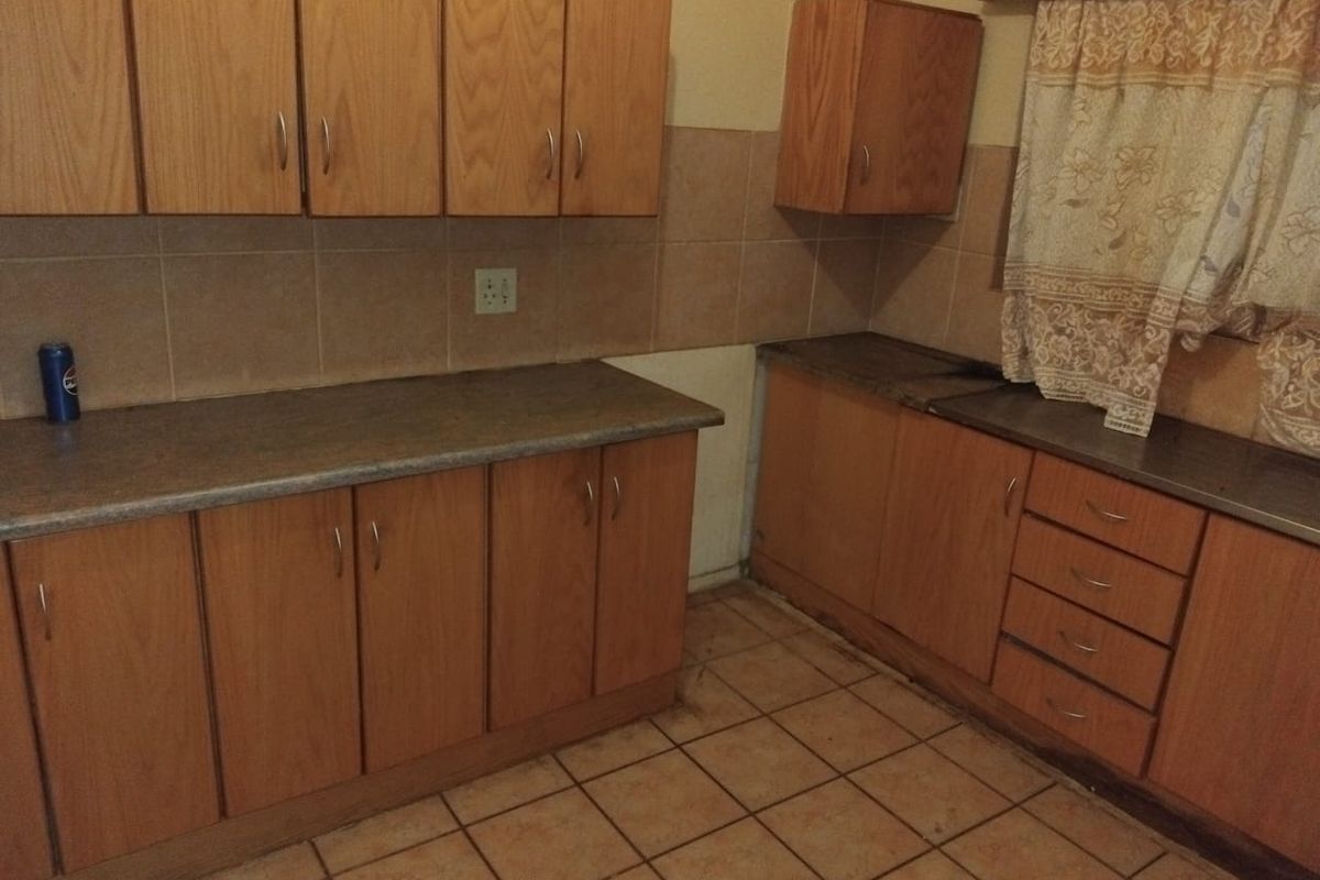 A dated kitchen featuring wood-look laminate cabinetry, tiled backsplash, and ceramic flooring, offering a blank canvas for a modern renovation.