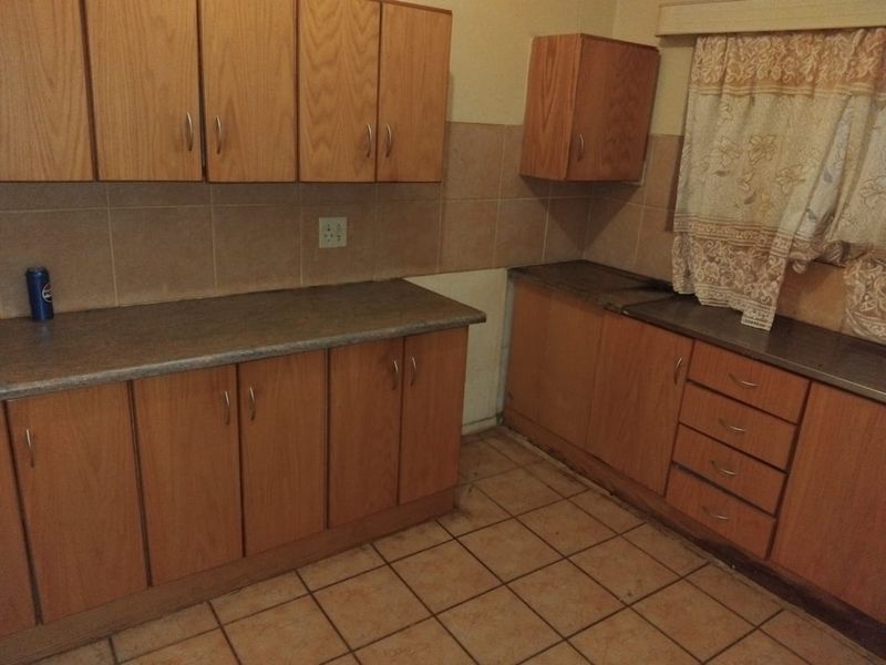 A dated kitchen featuring wood-look laminate cabinetry, tiled backsplash, and ceramic flooring, offering a blank canvas for a modern renovation.