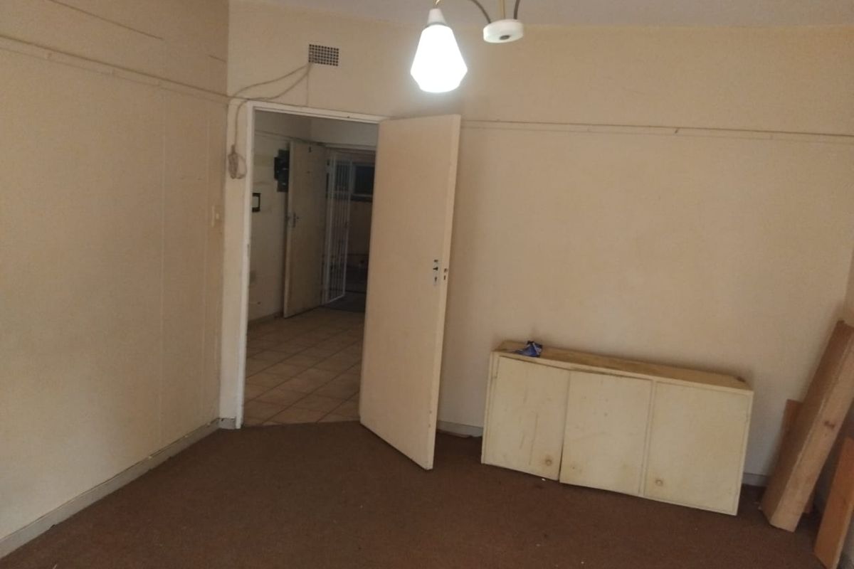 An empty living room featuring worn carpet flooring, dated wall finishes, and a built-in cabinet, requiring cosmetic updates to improve its overall appeal.