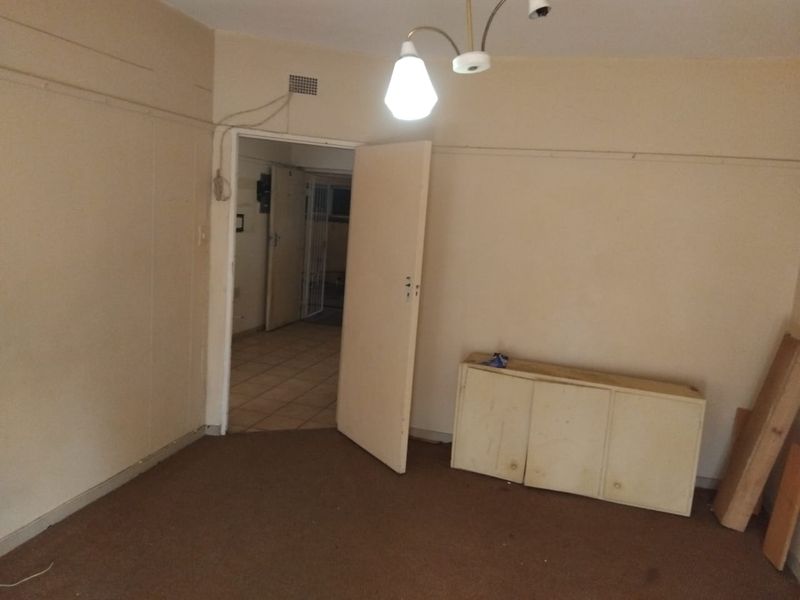 An empty living room featuring worn carpet flooring, dated wall finishes, and a built-in cabinet, requiring cosmetic updates to improve its overall appeal.