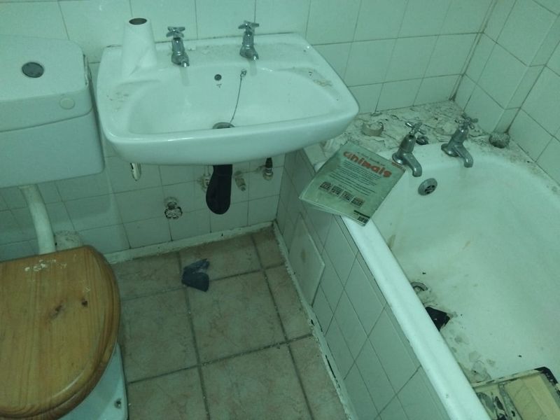 A dated bathroom featuring a wall-mounted basin, bathtub, and toilet, requiring significant renovation and repair to the tiled surfaces and fixtures.