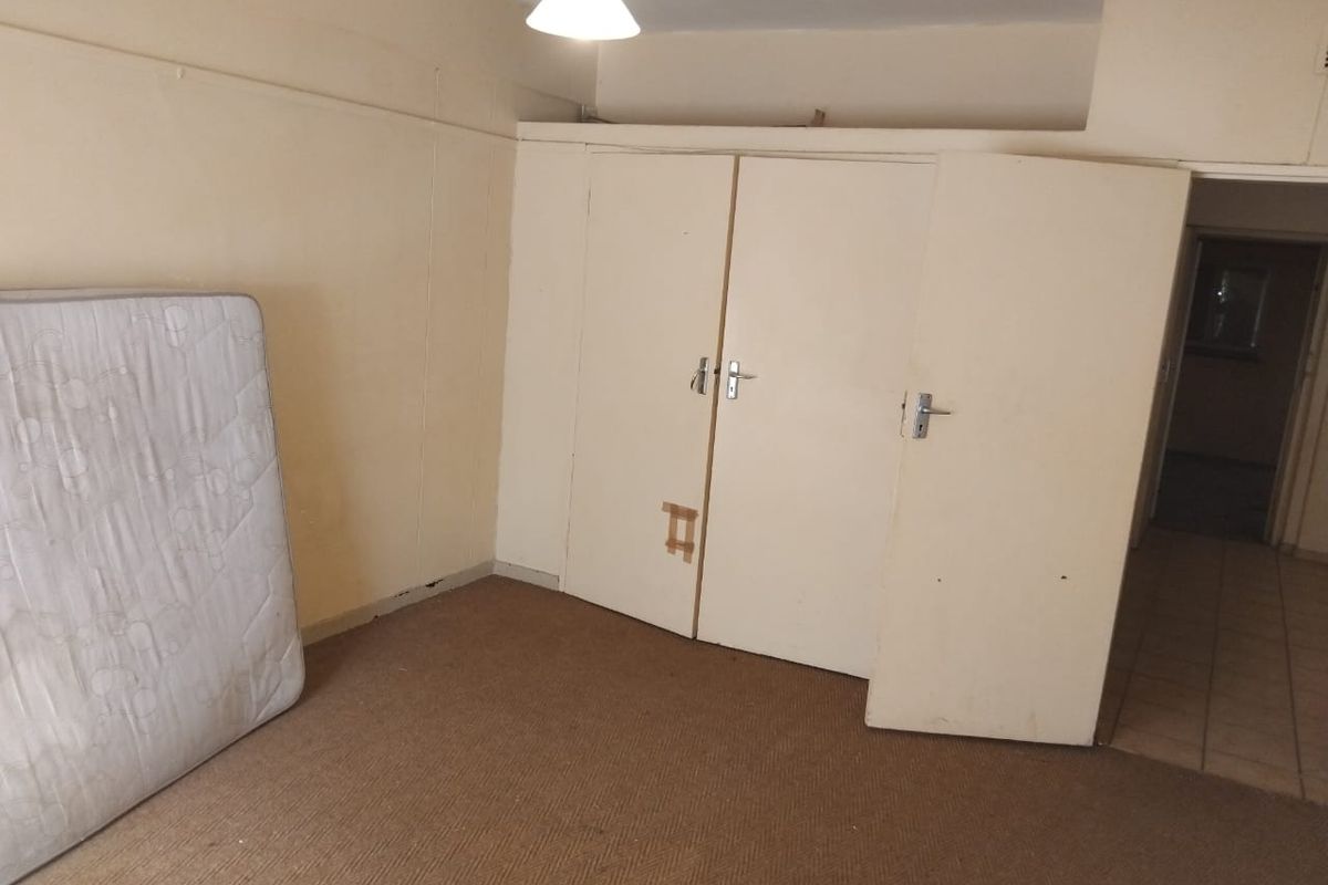 A bedroom featuring built-in cupboards and carpeted flooring, currently vacant and in need of cosmetic updates and repairs.