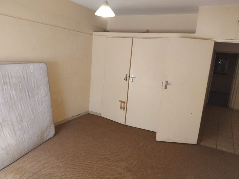 A bedroom featuring built-in cupboards and carpeted flooring, currently vacant and in need of cosmetic updates and repairs.