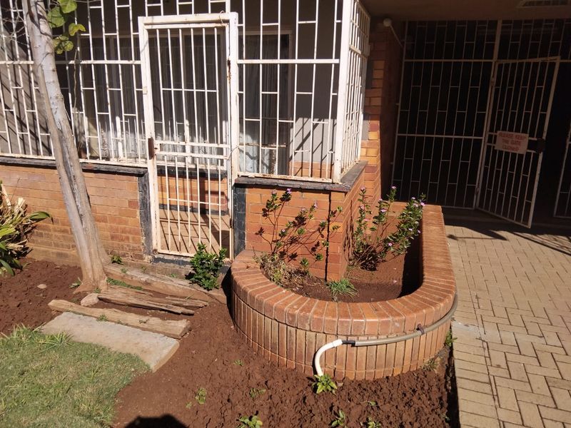 Front entrance area featuring a face brick facade, security gates, and a curved brick planter box along a paved walkway.