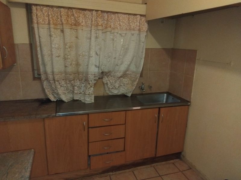 A dated kitchen area featuring laminate cabinetry, a stainless steel sink, and tiled splashbacks, requiring modernization to improve functionality and aesthetic appeal.