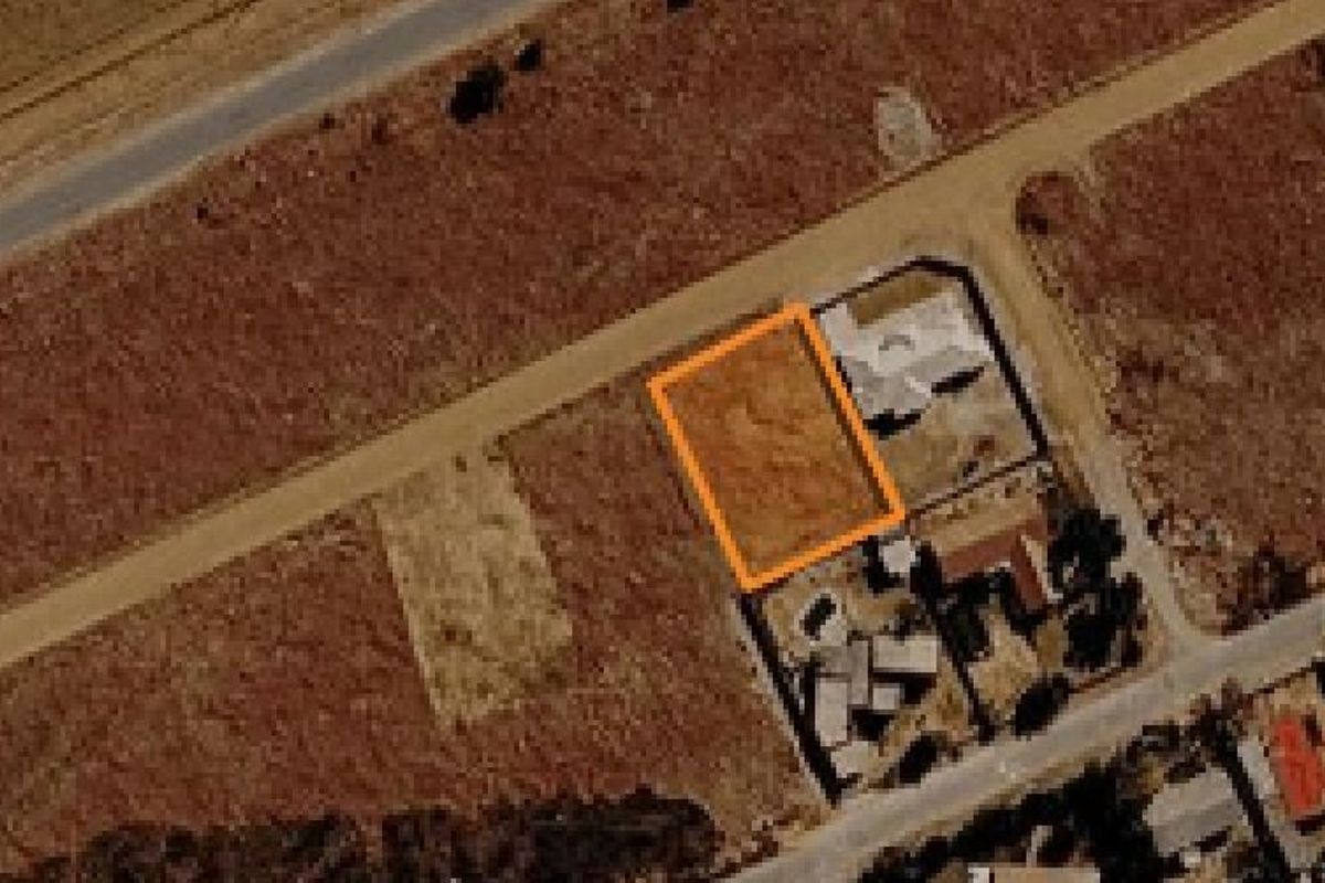 Aerial view of a vacant residential land plot highlighted in orange, situated in a developing neighborhood.