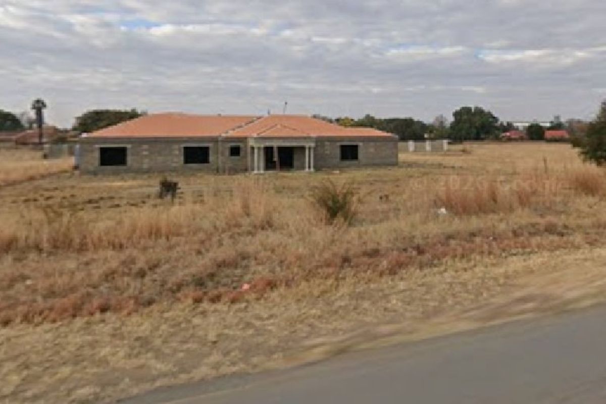A view of an unfinished residential property under construction, featuring masonry walls and a tiled roof, situated on a large vacant plot.