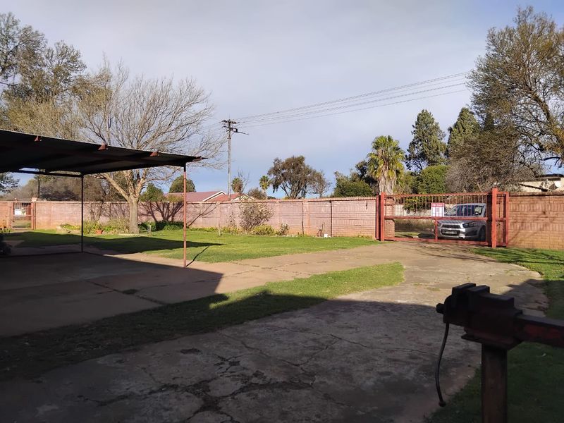 Spacious rear yard featuring a concrete driveway, metal carport, and secure perimeter brick walling with a gated entrance.